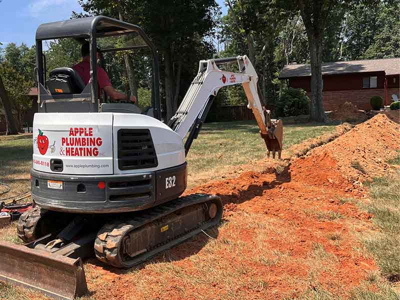 Apple Plumbing, Heating, & Air excavation equipment digging a trench in a yard.